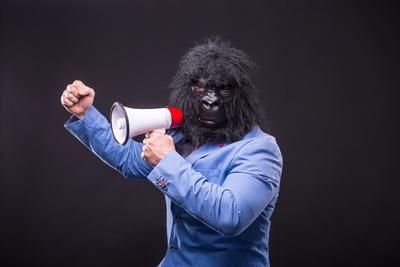 businessman wearing gorilla mask and screaming to megafon-stock-photo