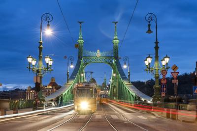 Trams crossing Liberty Bridge illuminated at night with the Gellert Hotel in the background, Budapest, Hungary-stock-photo