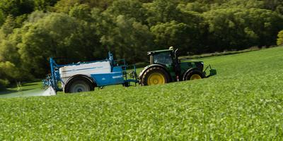 A farmer spraying on the spring wheat field with a John Deere tractor and a mamut topline sprayer. Panning shot.-stock-photo