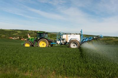 A farmer spraying on the spring wheat field with a John Deere tractor and a mamut topline sprayer. Panning shot.-stock-photo