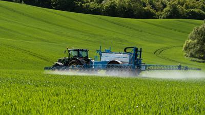 A farmer spraying on the spring wheat field with a John Deere tractor and a mamut topline sprayer.-stock-photo