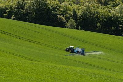 A farmer spraying on the spring wheat field with a John Deere tractor and a mamut topline sprayer.-stock-photo