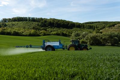 A farmer spraying on the spring wheat field with a John Deere tractor and a mamut topline sprayer. Panning shot.-stock-photo