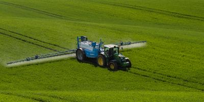 A farmer spraying on the spring wheat field with a John Deere tractor and a mamut topline sprayer.-stock-photo